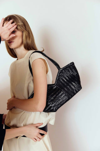 Woman holding a black woven handbag against a plain background