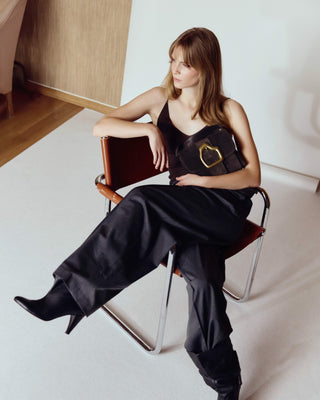 Woman in black outfit sitting on a chair in a minimalistic room.