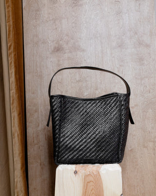A black leather bag on a wooden pidestall