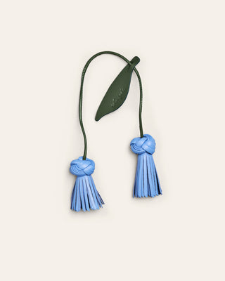 Decorative item with blue tassels and green leaf on a beige background