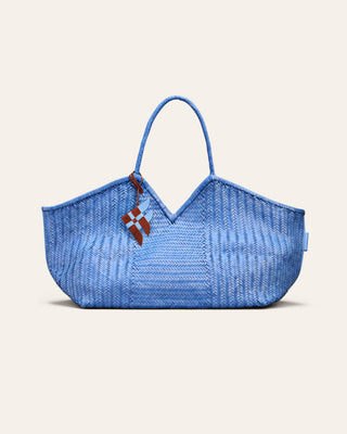 Cala Jade large blue woven shoulder bag with a fish shaped leather charm attached on a beige background
