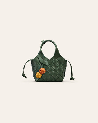 Green woven handbag with a cherry bag charm on a light beige background
