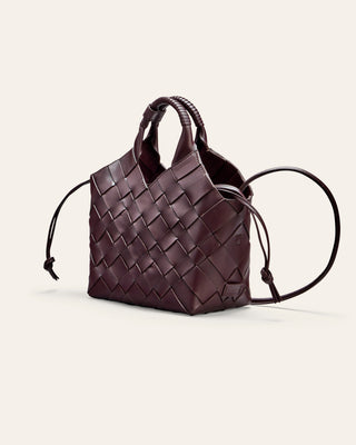 A burgundy woven leather bag on a beige background seen from the side