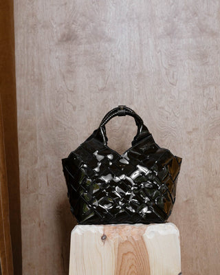 a brown patent leather bag on a wooden pidestal