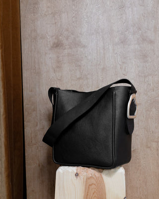 A black leather tote on a wooden pidestal