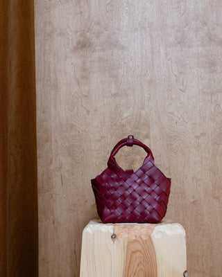 A burgundy leather bag on a wooden pidestal