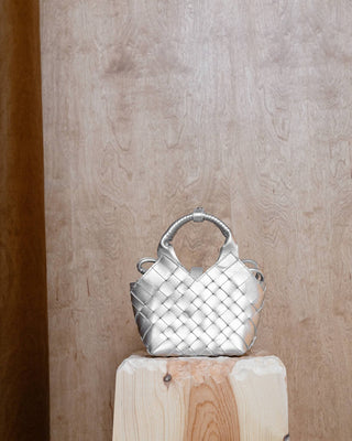 a silver colored leather bag on a wooden pidestal