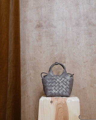 A beige woven leather bag on a wooden pidestal