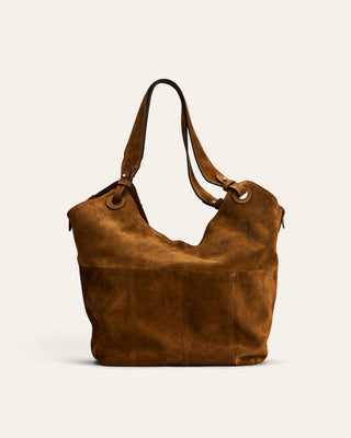 A brown suede hobo-style shoulder bag with a long strap and metal grommets, photographed against a plain off-white background.