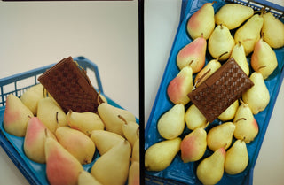 Basket of pears with a brown woven leather wallet on a white background